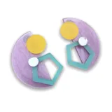 Par de aros colgantes con forma geométrica, hechos de acrílico. Cada uno tiene una base semicircular lila con textura, un círculo amarillo y un pentágono calado color verde agua.