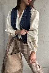 Chaleco de jean oscuro con tachas doradas aplicadas en la parte frontal y escote en V.