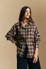 Camisa de estilo leñador con estampado de cuadros en tonos azul, negro y marrón. Presenta cuello clásico, cierre frontal con botones y mangas largas con puños abotonados.