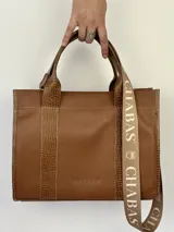 Cartera marrón de cuero genuino con doble asa corta y correa bandolera estampada con la frase "Chabas, soy real, no perfecta".