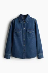 Camisa de denim supersuave color azul, con cuello, botones a presión en el frente y canesú en la espalda. Tiene bolsillos superiores con solapa y botón a presión, y mangas largas con botones a presión en los puños.