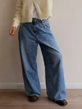 Pantalón de jean estilo palazzo en tono celeste medio, con corte amplio y recto. Presenta detalles de roturas sutiles en los bolsillos y ruedo, con cierre frontal y bolsillos laterales.