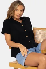 Camisa negra de lino de manga corta, con cuello camisero, cierre frontal con botones de madera y un bolsillo ojal en el pecho.