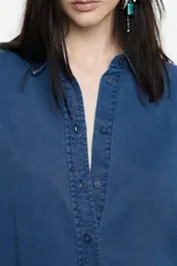 Camisa de manga larga color gris claro con efecto lavado, corte recto y botones frontales marrones. Presenta cuello camisero y pespuntes a contraste.