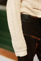 Buzo de tejido de punto color crudo, con cuello amplio que puede usarse caído sobre los hombros, mangas largas con trenzas de ochos y cuerpo con punto arroz.