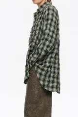 Camisa de corte recto y largo medio, confeccionada en tejido de algodón con textura. Presenta un diseño de cuadros en tonos rojo, negro y azul, cuello camisero, cierre frontal con botones, manga larga con puños abotonados y bolsillo de plastrón en el pecho.