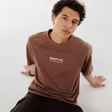 Remera marrón con mangas raglán y estampado con la leyenda "[NXT-K] NO LIMITS. NO HESITATIONS." en color blanco.