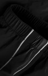 Pantalón deportivo de microfibra opaca, color negro, con diseño de vivos laterales blancos a contratono. Presenta cintura elástica y puños elásticos en los tobillos, con un pequeño logo bordado en la parte superior.