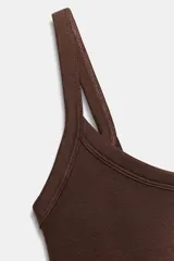 Body de cuello cuadrado con tirantes finos, confeccionado en tejido elástico con cierre inferior mediante botones a presión.