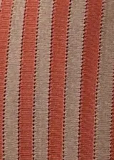 Vestido largo tejido a crochet, con rayas verticales color naranja y beige, sin mangas y con aberturas laterales.