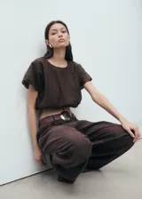 Blusa crop de color marrón, con cuello redondo y mangas cortas abullonadas con diseño estilo globo. Presenta un ajuste elástico en la cintura.