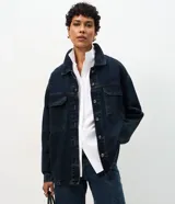 Campera tipo overshirt de denim en color azul oscuro, con corte amplio y largo extendido. Presenta cuello clásico, cierre frontal con botones metálicos, mangas largas y dos bolsillos delanteros con solapa.