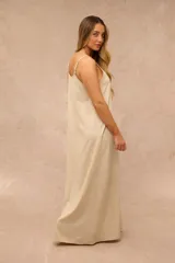 Vestido largo beige de corte recto y holgado, con tirantes finos y escote en V. Presenta un sutil estampado de flores en tono más claro a lo largo de la prenda.