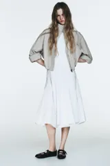 Vestido midi blanco, con cuello halter y falda con terminación en godets, lo que le da volumen y movimiento.