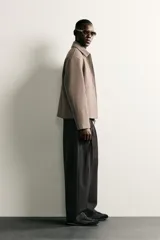 Pantalón de corte balloon fit en color gris oscuro, confeccionado en tejido con viscosa. Presenta pliegues frontales, cintura ajustable con cinturón integrado, bolsillos laterales y bolsillos traseros de doble vivo. Cierre frontal con cremallera y botón.