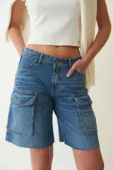 Bermuda de denim azul de tiro bajo, con múltiples bolsillos cargo en los laterales y terminación de ruedo deshilachada.