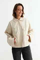 Campera de jean color crudo con diseño de corte holgado, cuello clásico, cierre frontal y detalles de desgastes en toda la prenda.