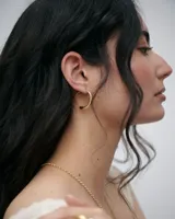 Aros de silueta orgánica con diseño continuo y cierre integrado, elaborados en plata con baño de oro.