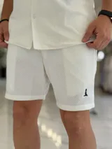 Bermuda blanca de tejido texturizado, con pequeño bordado oscuro en la parte inferior izquierda.
