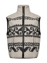 Chaleco de polar con diseño jacquard de motivos geométricos en tonos beige y gris oscuro. Presenta cuello alto, cierre frontal metálico con bordes de cuero sintético y bolsillos laterales con cierre.