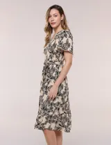 Vestido midi de rayón en color beige con estampado floral en negro, escote en V, pechera con punto smock, mangas cortas acampanadas con detalle de galón y falda evasé con volado en el ruedo. Incluye lazo textil ajustable en la cintura.