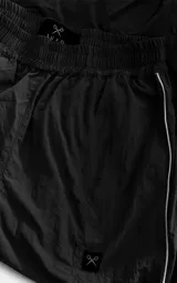 Pantalón deportivo de microfibra opaca, color negro, con diseño de vivos laterales blancos a contratono. Presenta cintura elástica y puños elásticos en los tobillos, con un pequeño logo bordado en la parte superior.