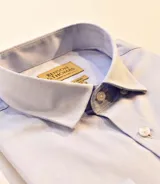 Camisa celeste de vestir, manga larga, con cuello clásico y botones blancos.