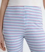Pantalón de pijama ajustado confeccionado en tejido ribana con elastano, estampado a rayas horizontales multicolor. Presenta cintura elástica y detalle de botones frontales decorativos.