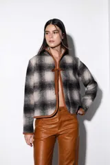 Chaqueta corta negra de paño con ribete de cuero color marrón en todo el contorno. Se ata con una tira de cuero en el centro y tiene dos bolsillos laterales.