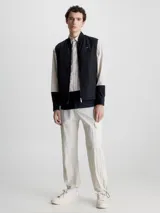 Chaleco negro acolchado con cuello alzado, cierre de cremallera, bolsillos con botón a presión y logo de Calvin Klein en el pecho.