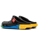 Zuecos Crocs de color negro, en colaboración con Lego, con tira trasera decorada con el logo de Lego y plataforma inspirada en bloques de construcción de colores azul, amarillo y verde.