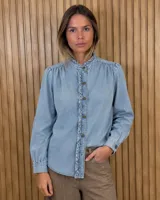 Camisa de jean lino color negro con cuello mao, mangas largas, frunces en los hombros, botonadura frontal y sutiles volados decorativos a lo largo de la botonadura.
