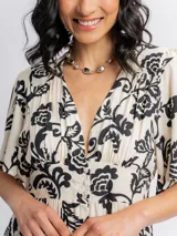 Vestido corto de viscosa en color beige con estampado floral en negro, escote en V con botones frontales, mangas cortas y falda amplia con volados en capas.