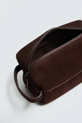 Neceser de mano fabricado en piel con acabado de serraje, cuenta con compartimento principal con cierre de cremallera, bolsillo interior con cierre y asa lateral.