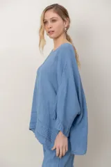 Blusa de lino color verde militar, holgada, de manga 3/4 con volados en los puños, cuello redondo y detalle de alforzas horizontales en el dobladillo.