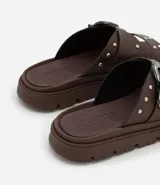 Sandalia plana negra con dos tiras anchas sobre el empeine, una con hebilla metálica estilo western y tachas plateadas.