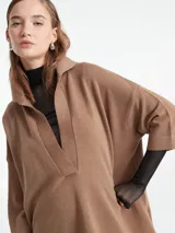 Poncho tejido de punto color negro con escote en V y cuello tipo polo. Presenta un diseño holgado con mangas tres cuartos.