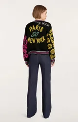 Cárdigan de punto negro con cuello en V y cierre frontal con botones. Presenta estampado de flores, corazones y números en colores amarillo, rosa y verde.