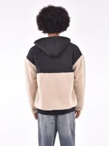 Campera con cierre frontal, capucha y diseño de bloques de color. La parte principal del cuerpo y las mangas son de tejido de borrego (teddy) color beige claro, mientras que los hombros, la capucha y los bordes son de tela negra lisa.