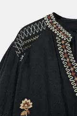 Camisa negra de manga larga con cuello redondo y escote en V, adornada con bordados florales en contraste en tonos beige y marrón a lo largo de la abertura frontal, hombros y mangas.