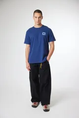 Remera de manga corta color gris, con cuello redondo y un pequeño parche cuadrado con una cruz estampada en el pecho.