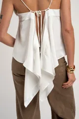 Blusa blanca de satén, corte al cuerpo con escote en V y tirantes finos. Presenta un diseño cruzado en los laterales con tiras largas para atar.