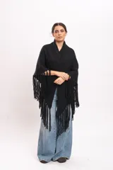 Triángulo tejido artesanalmente en telar manual con hilado mecha de lana merino, de color negro, con diseño envolvente y flecos largos en los bordes.