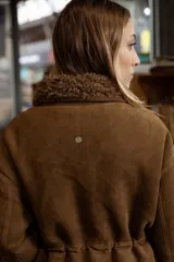 Campera de efecto gamuza color tostado con interior de corderito sintético. Presenta cierre frontal, bolsillos delanteros con solapa, cintura ajustable con cordón y puños con detalle de corderito.