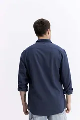 Camisa de manga larga color azul marino con textura, cuenta con cuello clásico, cierre frontal con botones y un bolsillo en el pecho.