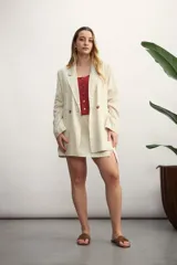 Blazer de mujer color rosa pálido, de corte recto y largo, con solapas de muesca y un solo botón frontal marrón. Presenta bolsillos de parche en la parte delantera y mangas tres cuartos.