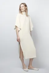 Vestido midi fluido de cuello alto y manga corta tipo capa. Presenta un diseño minimalista con bajo recto y aberturas laterales, con cierre en la espalda.