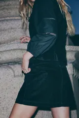 Pollera mini de denim negro con tiro bajo, cierre frontal y dos bolsillos delanteros tipo cargo. Presenta botones decorativos con detalles de strass en la cintura y en las solapas de los bolsillos.