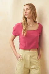 Top crop color fucsia con escote cuadrado y mangas cortas con detalle de lazos. Presenta una tela con textura sutil y calce entallado.