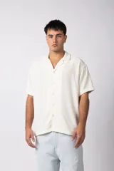 Camisa de manga corta con cuello cubano, confeccionada en lino entramado de textura natural. Presenta un corte relajado y cierre frontal con botones.